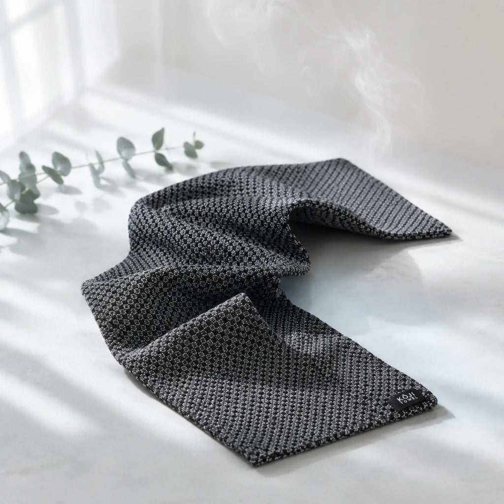 Exfoliačný uterák Kōji Face Towel rozvlnený na svetlom pozadí